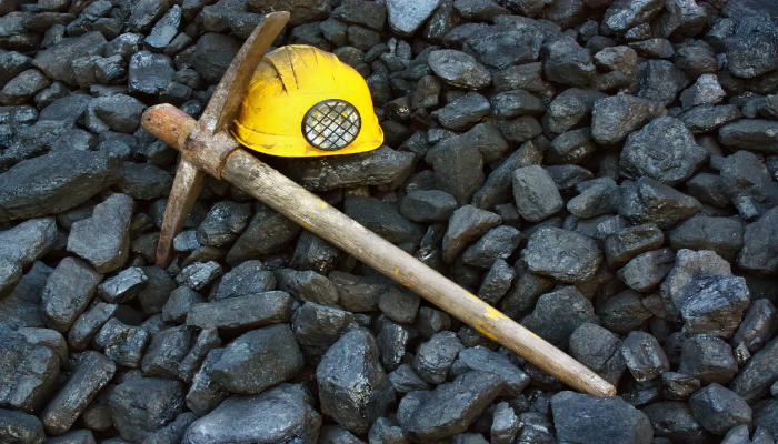 yellow hard hat next to ax on a bed of black coal